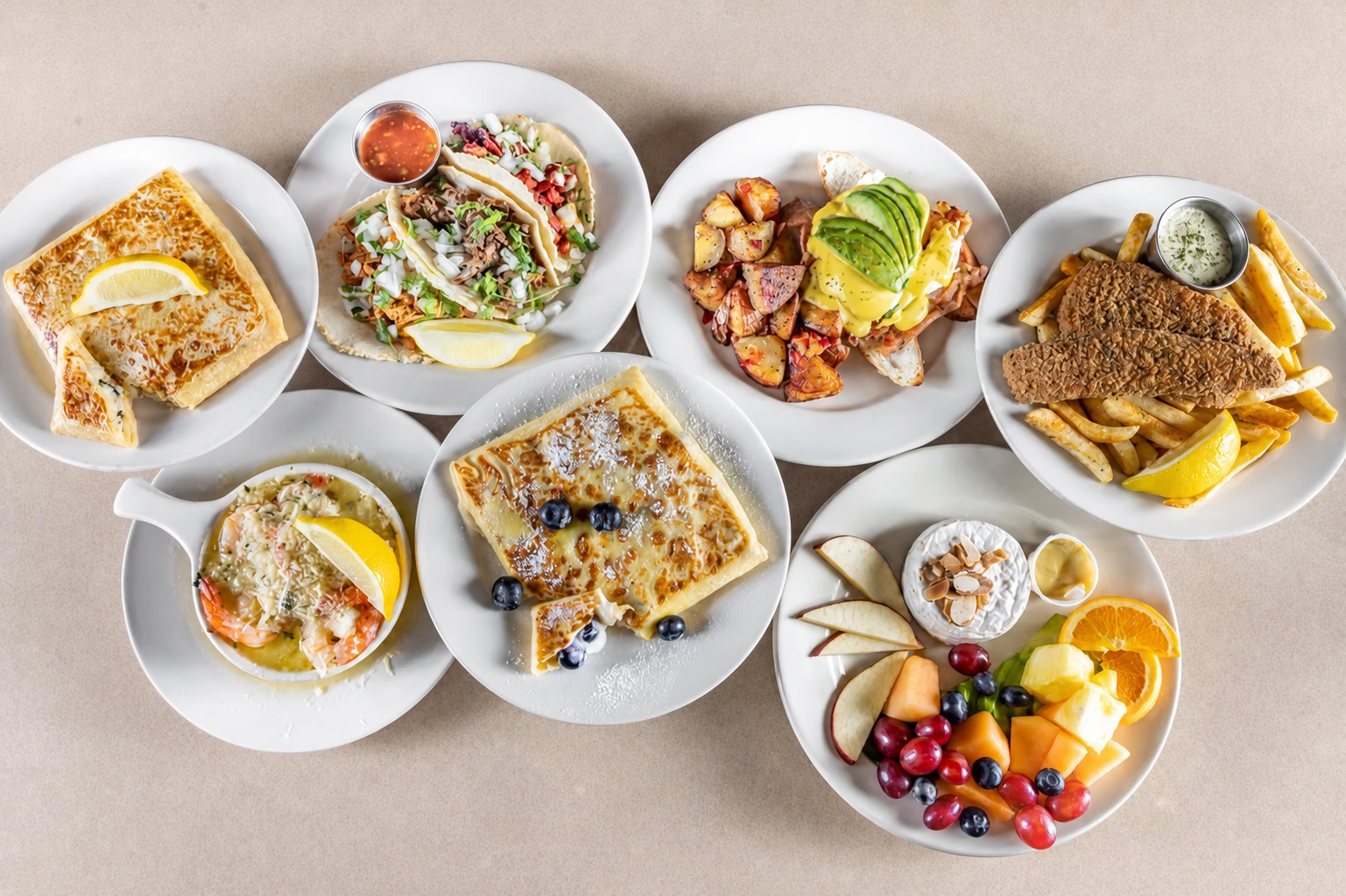 A table spread of crepes, tacos, eggs Benedict, fish, shrimp, and fresh fruit